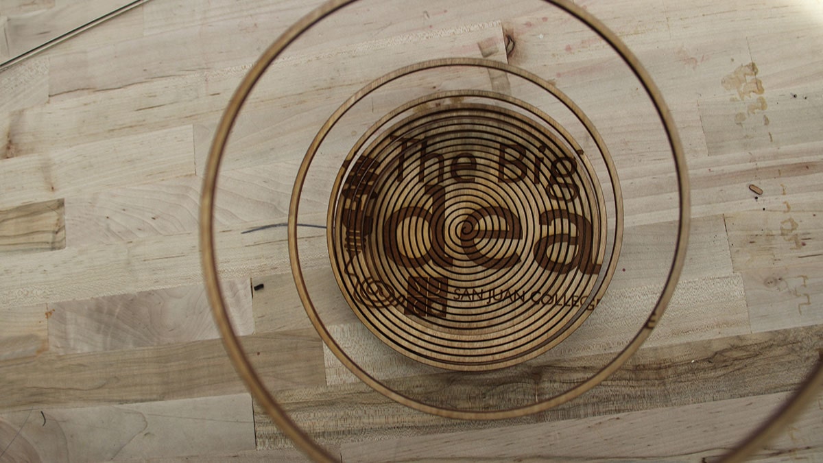 A piece of wood laser cut into a spiral with The Big Idea @ San Juan College engraved into the wood.