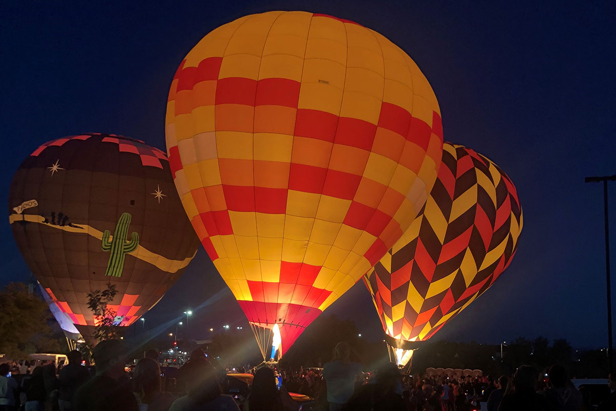 Three large hot air balloons full lit up from the flame at night.