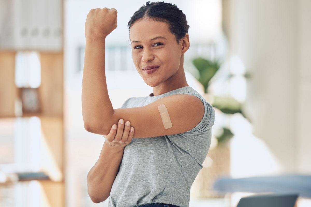 Women flexing her arm with a band aide from a shot.