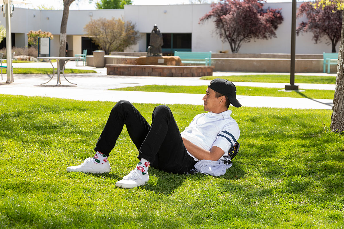 Student sitting in the grass on the SJC campus leaning on his backpack