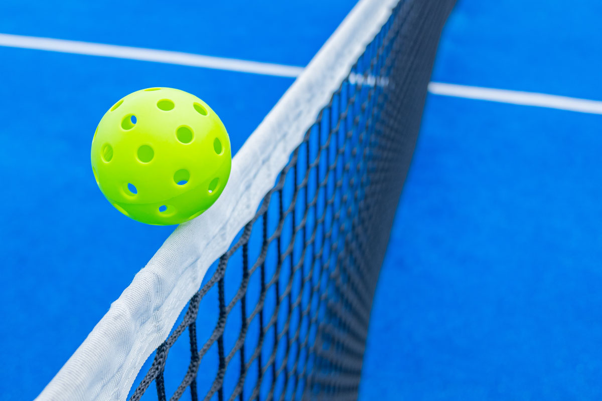 A bright yellow pickleball grazing over a net on a blue court.