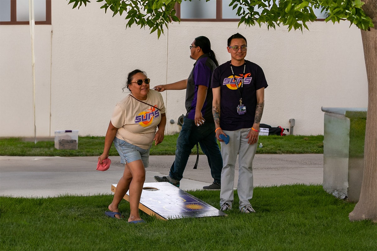 Three students in SJC SUNS gear playing cornhole