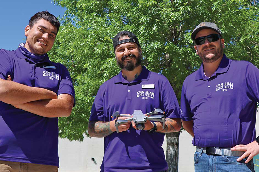 Three men wearing purple shirts standing holding a drone