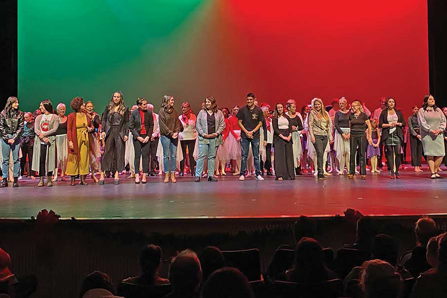 Indoor theater stage full of performers with red, green, and black colored background