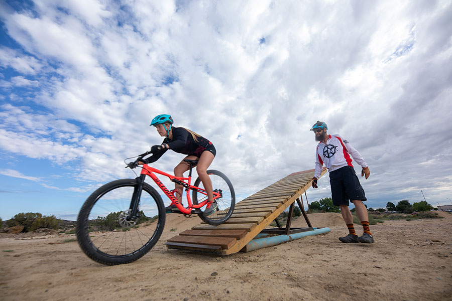 Women on her bicycle coming off a teeter ramp with a gentleman guiding her